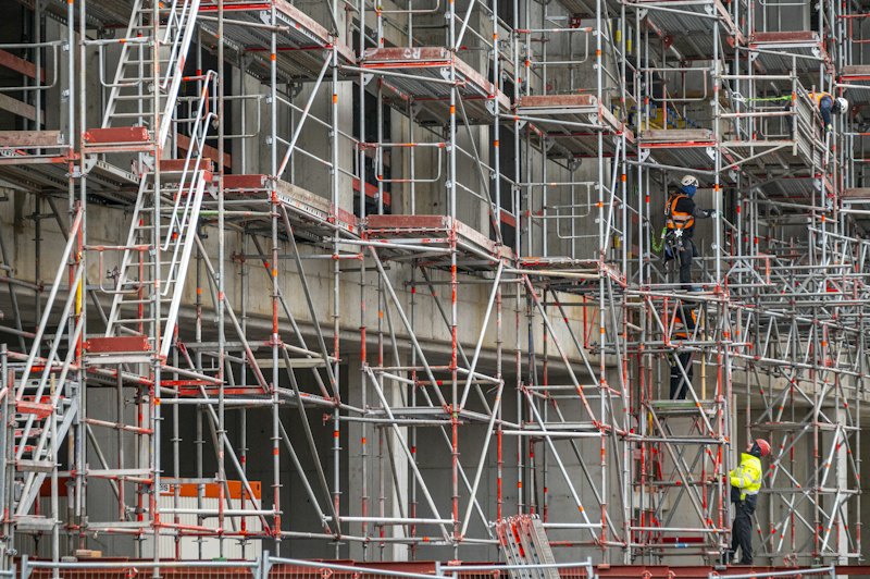 Πρόσοψη κτιρίου καλυμμένη με ικριώματα, σκάλες και εργαζόμενους με ανακλαστικά γιλέκα