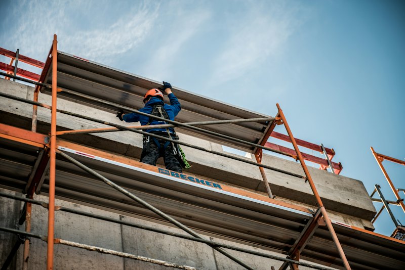 Τεχνίτης με κράνος εργάζεται πάνω σε σκαλωσιά στην πρόσοψη κτιρίου